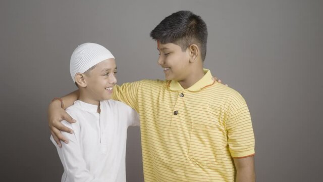 Happy Hindu Muslim kids showing unity by holding hands together by looking at camera on gray background - concept of diversity, bonding and multiethnic friendship.