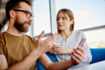 Handsome male blogger communicate during friendly meeting with Caucasian best friend discussing mobile publication, millennial man and woman spending weekend leisure together in coffee shop