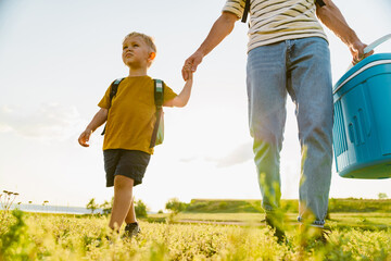Young white father and son walking with cooler bag across summer field