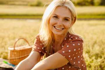Blonde mature woman smiling during picnic on field - Powered by Adobe