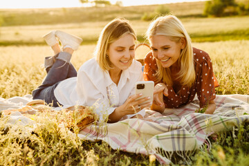 White mother and daughter using smartphone during picnic on field