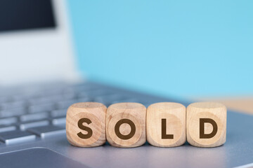 Wooden cube with SOLD text on laptop keyboard background, Business and finance concept.