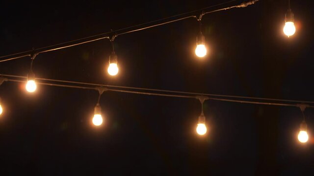 Many lamp bulbs glowing in darkness of night outdoors under falling snow flakes in winter