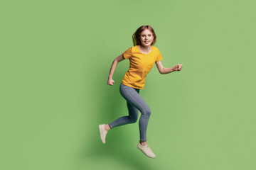 Fototapeta na wymiar Portrait of charming cheerful lady jump run hurry wear yellow t-shirt jeans sneakers on green background