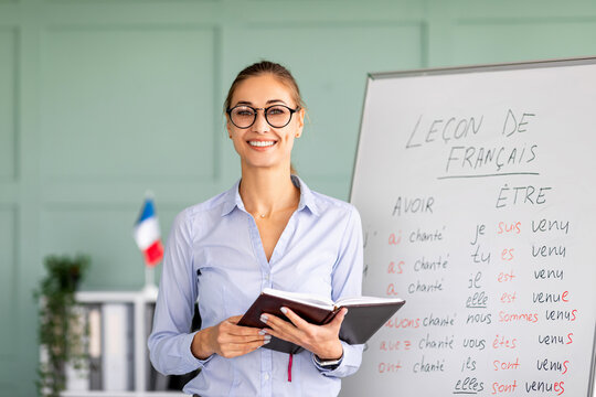 Learning and knowledge concept. Young smiling woman posing near whiteboard with French language grammar rules