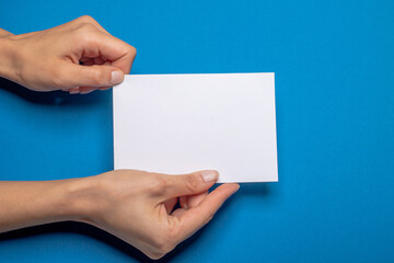 two female hands holding a blank piece of paper with copy space in front of a blue colored background cardboard
