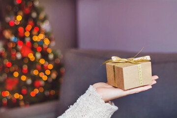 Hand holding Christmas gift box on a tree bokeh lights background