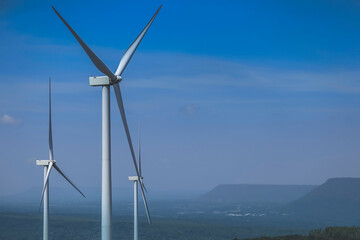 The big white wind turbine for spinning electricity sees large mountains far away, with clouds and...