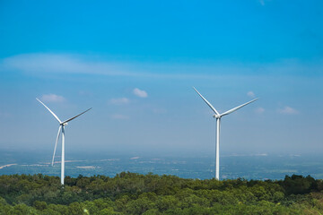 The big white wind turbine for spinning electricity sees large mountains far away, with clouds and blue skies above the mountains.