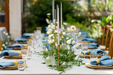 Banquet wedding table setting with blue napkins, gold cutlery, crystal, fresh flowers and candles. Wedding decorations. Soft selective focus.