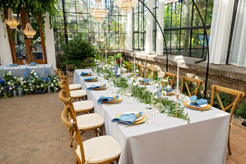 Banquet wedding table setting with blue napkins, gold cutlery, crystal, fresh flowers and candles. Wedding decorations. Soft selective focus.
