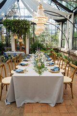 Banquet wedding table setting with blue napkins, gold cutlery, crystal, fresh flowers and candles. Wedding decorations. Soft selective focus.