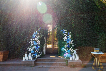 Wedding arch for the ceremony, decorated with fresh white roses, blue orchids and candles. Wedding decor. Soft selective focus.