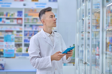 Man in white coat with tablet in pharmacy