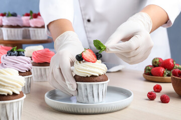 Pastry chef decorating sweet cupcake with mint at light wooden table, closeup