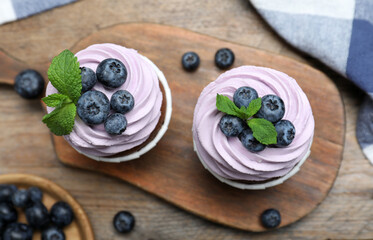 Sweet cupcakes with fresh blueberries on wooden table, flat lay