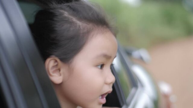 Slow motion scene ofA 4-5 year old Asian girl is sitting in a car looking out of the side mirror.