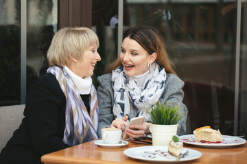 Family, an adult mother and daughter are sitting at a wooden table in a cafe on the street, looking at each other, smiling and holding hands