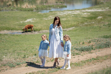 Young mother and her twin daughters are walking along a path in the village