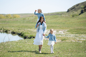 Naklejka na ściany i meble Mother and her twin daughters walk along a path near a reservoir in the village