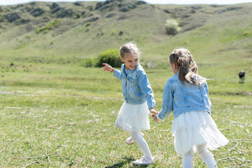Naklejka premium Two little twin sisters run and spin in the meadow