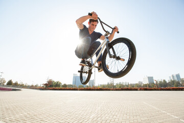 Street portrait of a bmx rider in a jump on the street in the background of the city landscape and the sun