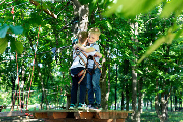 Two cute boys in an adventure park are doing rock climbing or passing obstacles on a rope road,...