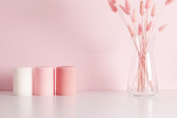 Three candles mockup on pink table, against pink wall with dry pink flowers.