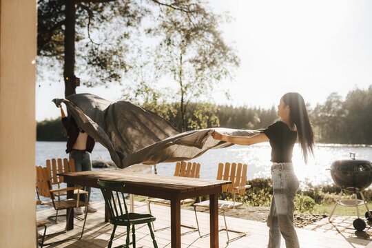 Young female friends placing tablecloth on table during social event