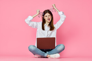 woman sitting on floor with laptop shopping entertainment pink background