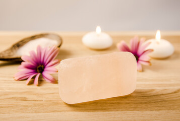 Bar of orange color exfoliating Himalayan crystal Salt Soap on wooden background with wooden spoon with pink Himalayan crystal Salt grains on spoon, decorated with candles and flowers.