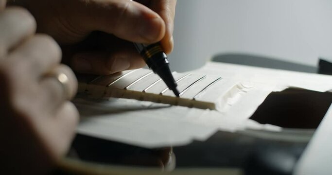 Luthier marks frets on the guitar by black marker before sanding, musical instruments repair shop, 4k 60p 10 bit
