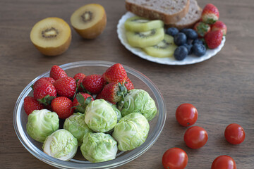 Fresh raw organic berries and exotic fruits in round glass plate on wooden table. cabbage,,kiwi, strawberry.
