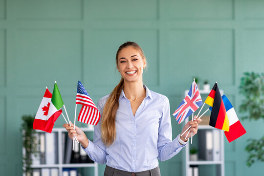 Foreign language studying school. Happy female tutor holding bunches of diverse flags, posing in office interior