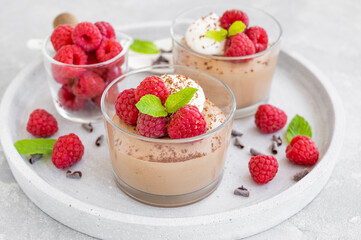 Chocolate mousse with whipped cream and fresh raspberries in a glass on a gray concrete background. Copy space.