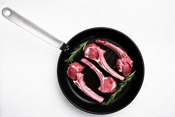 Raw lamb meat chops steaks, on frying cast iron pan, on white stone table background, top view flat...