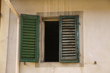 Fototapeta na wymiar Green shutters on the window against a yellow colored wall. Old exterior in italian mediterranian village with closed Wooden vintage window with green blinds.