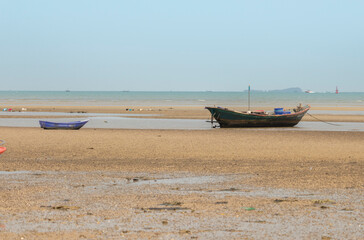Obraz premium fisherman's fishing boat on sand at a fishing village beach There is an island and sea background with the daytime sky. stranded fishing boat After the sea has receded