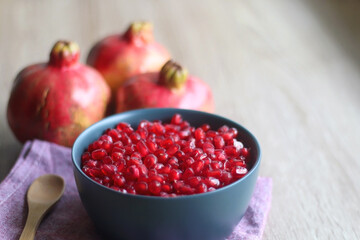 Bowl filled with pomegranate seeds and pomegranate fruit on a table. Selective focus.
