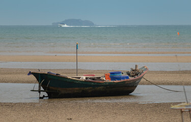 Obraz premium fisherman's fishing boat on sand at a fishing village beach There is an island and sea background with the daytime sky. stranded fishing boat After the sea has receded