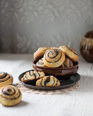 Fresh bread rolls buns with poppy seeds in ceramic bowl on light linen tablecloth, selective focus.