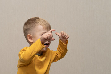 Cute boy in yellow t-shirt blond European German age 3 years isolated on gray background shows and...