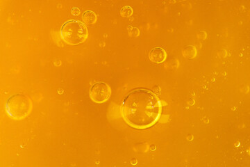 Texture of transparent yellow gel with air bubbles and waves on orange background. Concept of skin moisturizing, body care and prevention of covid19. Liquid beauty product closeup. Backdrop, flat lay