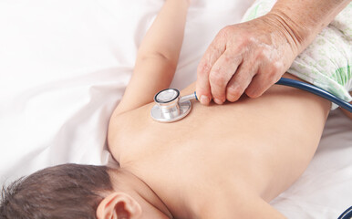 Doctor examining baby boy on bed with stethoscope.