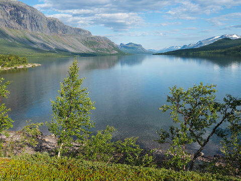 Beautiful moring on the shore of lake Lulealven, Lule river dam in Saltoluokta in Sweden Lapland. Reflection of mountains, tree and sky with dramatic clouds in clear calm water. Summer northern