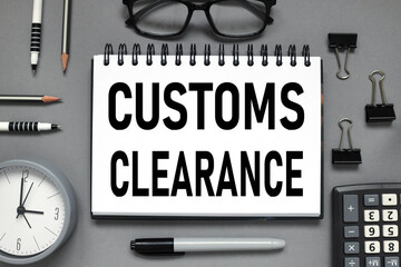 Customs Clearance . text on white paper. the inscription on the notebook. business concept. notepad on a gray background. glasses, pen, pencil, watch, calculator