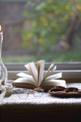 Plate of chocolate chip cookies, cinnamon sticks, soft blanket, open book and lit candles. Hygge at home. Selective focus.