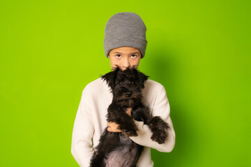 Child boy with a schnauzer puppy isolated over green background.