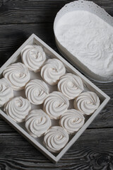 Homemade marshmallows on a tray. Zephyr in powdered sugar, lying in rows. On the surface of black pine boards.