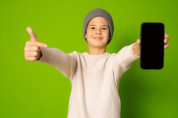 Joyful boy holding a phone and pointing isolated on green background